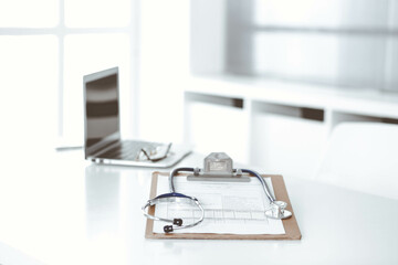 Stethoscope and clipboard with medication history records are on the table at the doctor's working place. Medicine and health care concept