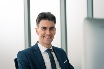 Fototapeta premium Adult smart business man in suit outfit sitting and working in front of computer with happy and smile in modern office