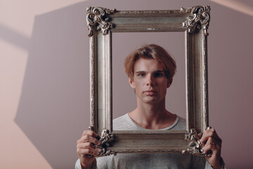 Millenial young man artist with blonde hair on gilded picture frame portrait.