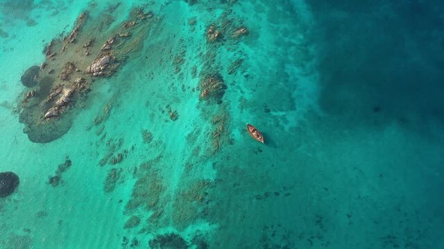 View from above, stunning aerial view of a wooden boat anchored to some rocks bathed by a crystal clear, turquoise water. Giardinelli island, La Maddalena Archipelago, Sardinia, Italy.