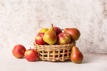 Basket with ripe pears and apples on light background