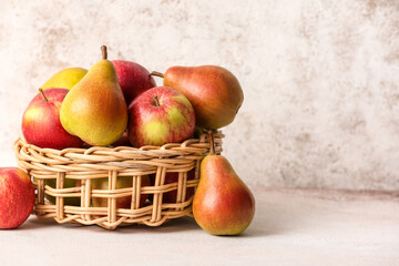 Basket with ripe pears and apples on light background