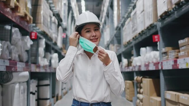 Asian woman inspector wearing safety hardhat and Face mask to prevent COVID-19 in warehouse. Worker in Factory safety measure  and keeping distance from work. Concept Blue collar health