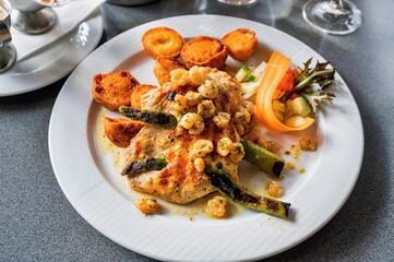 Chicken steak with asparagus and shrimp, fried halved potato, vegetable on plate.