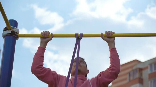 A young man performs pull-up exercises with fitness elastic bands on the street. Street training