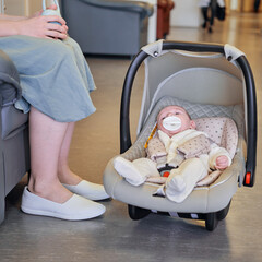 A mother with a newborn baby in a carrier is waiting for a doctor appointment in the lobby of the...