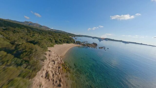 FPV video, view from above, aerial view from an FPV drone flying at high speed over a green and rocky coastline with some beaches bathed by a turquoise, crystal clear water. Sardinia.