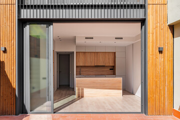 View from the sunny terrace to the interior of refurbished apartment. Modern kitchen interior with island and wooden furniture. .