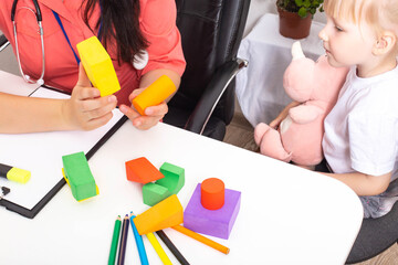 The doctor shows the multi-colored figures of the constructor to a little girl 3-4 years old. Development of thinking and logic in children, close-up