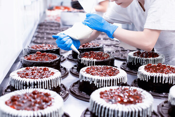 Female confectioner decorates sponge chocolate cakes with fresh cherry berry cream. Cake Making...