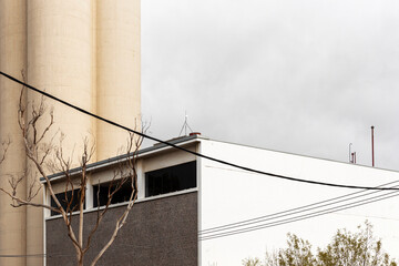 Electricity wires and leafless tree near factory.