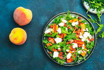 Grilled peach salad with feta cheese, hazelnuts and arugula on blue background, top view, copy space