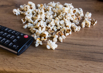 Popcorn scattered on a wooden table with a black remote control to the TV