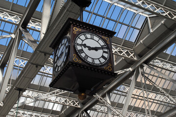 Large Ornamental Public Clock Hanging in Railway Station Forecourt seen from below  - obrazy, fototapety, plakaty