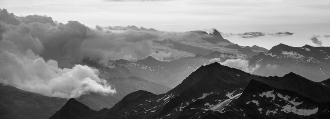 Rocky alpine mountains morning panorama. Cloudy sunrise on summer day. Grossglockner Mountain, Hohe Tauern National Park, Austrian Alps. Black and white image.