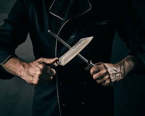 Chef sharpening a knife or cleaver on a metal file - obrazy, fototapety, plakaty