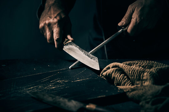 Chef sharpening a large knife on a handheld metal file