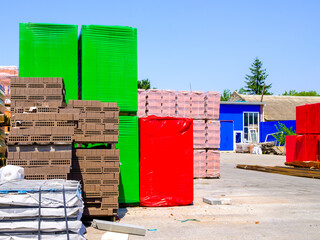 Stacked bricks and other building materials in bright packaging on the construction site on a sunny day.