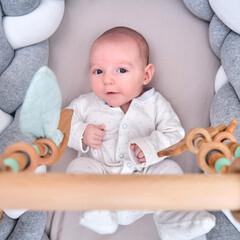 Smiling infant baby boy playing with a wooden mobile suspended above the crib. Happy child playing in bed with toys
