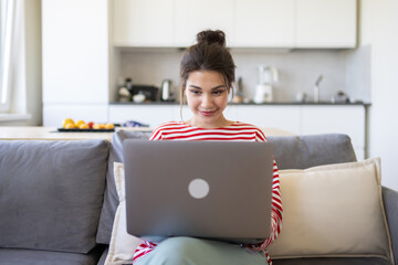 Smiling caucasian girl student professional employee working on laptop sitting on sofa at home...
