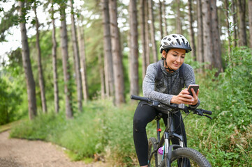 Fototapeta na wymiar Woman cyclist in the public park using smartphone