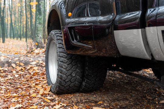 Close-up detail bottom pov view of dual twin offroad performance wheel of super heavy duty pickup truck car at autumn forest countryside driveway. Autumn weather woods offroad vehicle drive