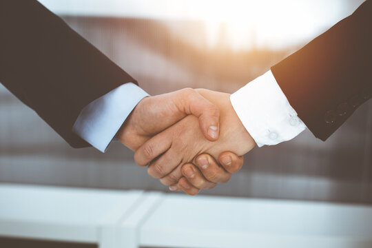 Businessman and woman shaking hands in sunny office, close-up. Concept of handshake as success symbol in business