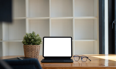 Mock up of blank screen tablet with keyboard on wooden desk at home office