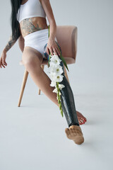 Disabled tattooed woman with prothesis leg sitting with flowers at the chair