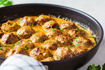 Swedish meatballs in creamy sauce in black frying pan, gray background. Scandinavian food concept.