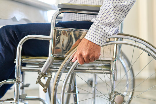 Hand von Senior nach Schlaganfall am Rad vom Rollstuhl
