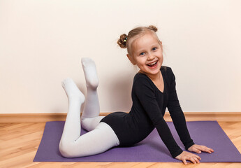 Smiling little ballerina training at home on the floor. Child in black leotard on purple mat