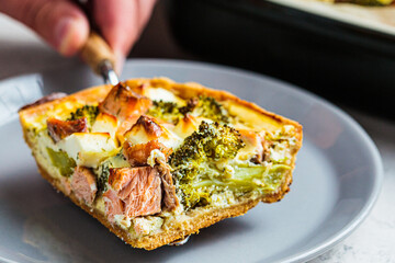 Piece of quiche pie with salmon and broccoli in plate.