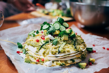 Messy food table with soft focus colorful vegetarian healthy dish - tortilla pie with pomegranate and avocado, cucumber and cheese