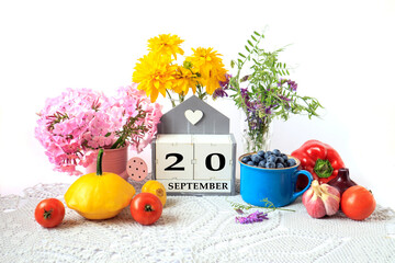 Calendar for September 20 : the name of the month in English, cubes with the number 20, ripe vegetables, bouquets of various flowers, blueberries in a blue cup on a gray napkin, white background