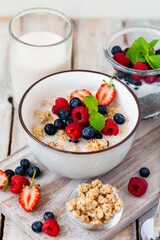 Bowl with vegan granola with fresh ripe organic berries, plant milk, mint. Concept of dieting, detox, tasty simple super food, healthy low calories breakfast. Wooden background, close up