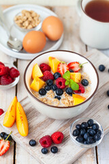 Bowl with vegan granola with fresh ripe organic berries, peach, plant milk, mint. Concept of dieting, detox, tasty simple super food, healthy low calories breakfast. Wooden background, close up