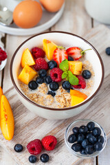 Bowl with vegan granola with fresh ripe organic berries, peach, plant milk, mint. Concept of dieting, detox, tasty simple super food, healthy low calories breakfast. Wooden background, close up