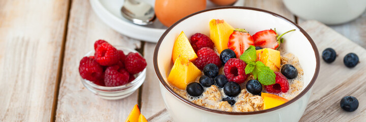 Bowl with vegan granola with fresh ripe organic berries, peach, plant milk, mint. Concept of dieting, detox, tasty simple super food, healthy low calories breakfast. Wooden background, close up banner