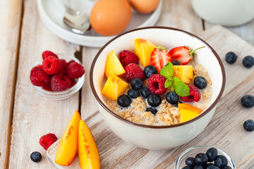 Bowl with vegan granola with fresh ripe organic berries, peach, plant milk, mint. Concept of dieting, detox, tasty simple super food, healthy low calories breakfast. Wooden background, close up