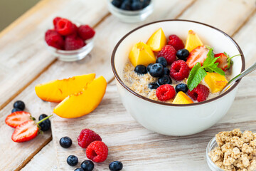 Bowl with vegan granola with fresh ripe organic berries, peach, plant milk, mint. Concept of dieting, detox, tasty simple super food, healthy low calories breakfast. Wooden background, close up