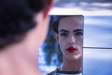 Young adult Hispanic transsexual girl looking in a mirror as a child after applying makeup. Transgender concept, inclusion and diversity. - obrazy, fototapety, plakaty