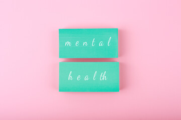Creative flat lay with blue blocks with written mental health text on bright pastel pink background. Concept of world mental health day, mental health assessment and awareness