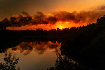 Black smoke against the background of a bright flaming sunset .