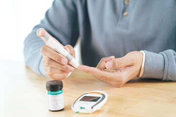 Asian man using lancet on finger for checking blood sugar level by Glucose meter, Healthcare and Medical, diabetes, glycemia concept