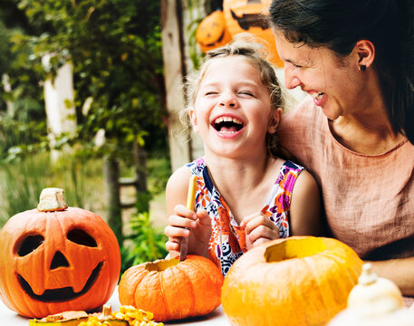 Young cheerful girl carving pumpkins with her mom