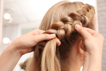 Professional stylist braiding client's hair in salon, closeup
