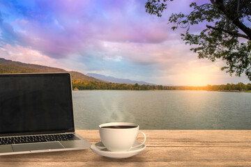 A laptop and a coffee cup on wood table in the nature background.