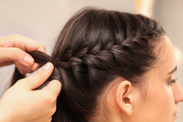 Naklejka premium Professional stylist braiding client's hair on blurred background, closeup