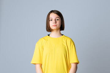 Portrait of beautiful cute teen girl in yellow casual tshirt looking at camera, standing over light...